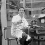 Black and white photo of a man at the work bence in the factory by Derrick Saines