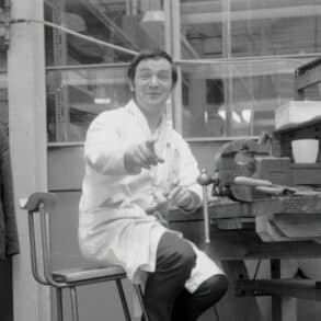 Black and white photo of a man at the work bence in the factory by Derrick Saines