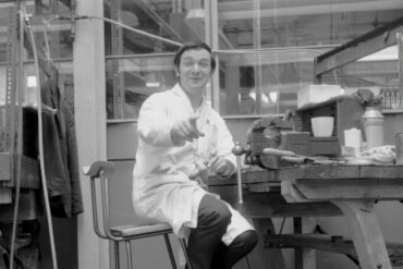 Black and white photo of a man at the work bence in the factory by Derrick Saines