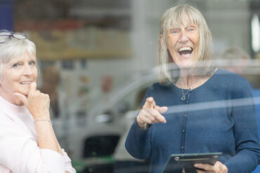 Photo taken from outside through the glass of two women talking at the Ronson Reunited event