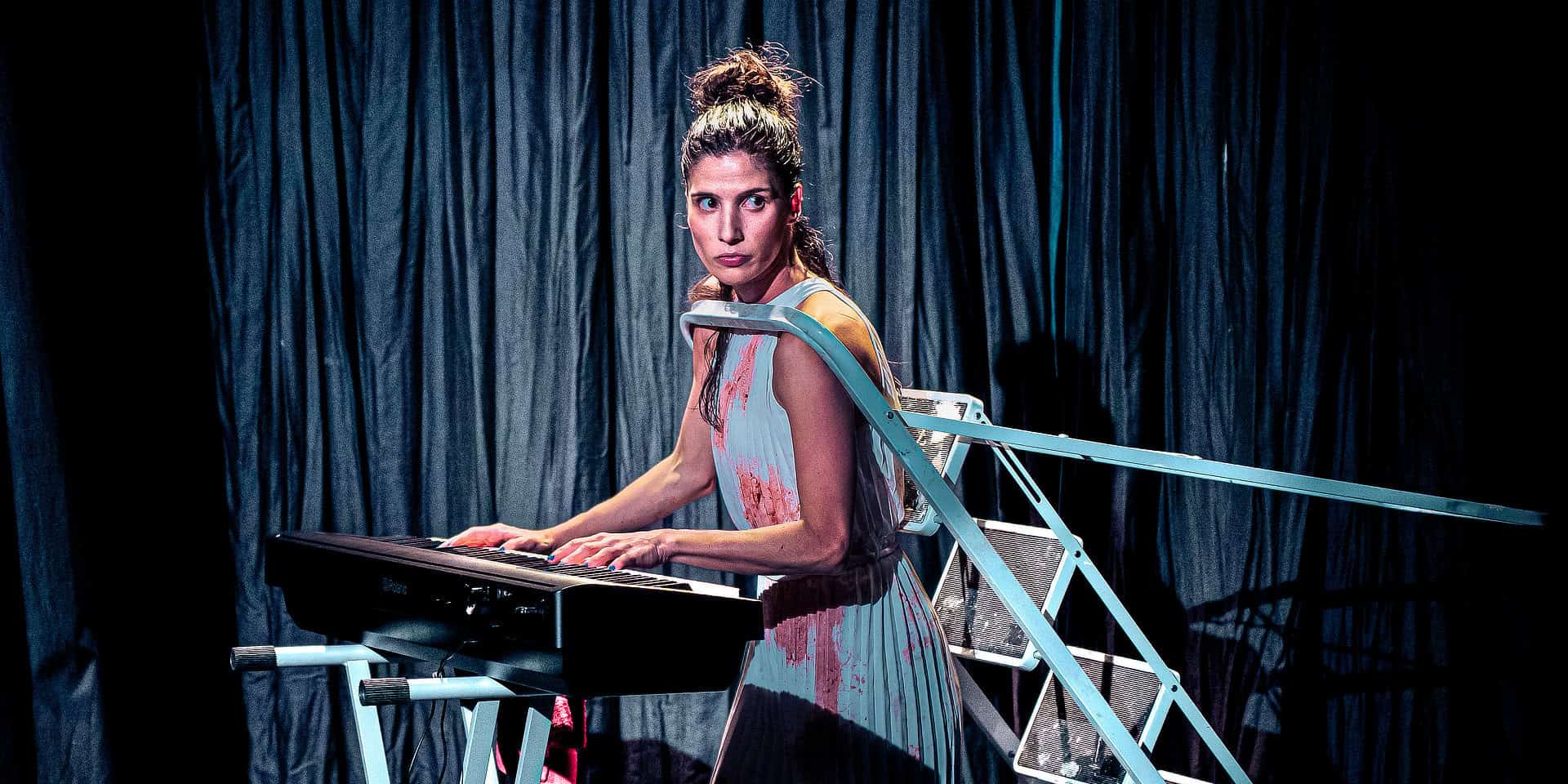Gabriela Flarys performing Deluge on stage - playing an organ whilst having her head through a stepladder