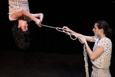 Two women performing on stage with rope entwining them