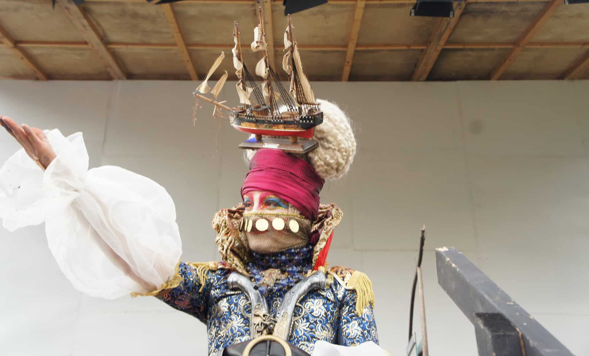 Woman on stage dressed extravagantly and with a ship on her head