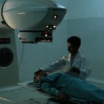 Patient lying on a Radiotherapy machine bed with nurse standing next to them