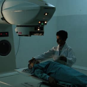 Patient lying on a Radiotherapy machine bed with nurse standing next to them