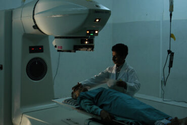 Patient lying on a Radiotherapy machine bed with nurse standing next to them