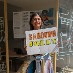 Tracy outside Boojum and Snark with a sign that reads 'sandown jolly'