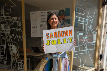 Tracy outside Boojum and Snark with a sign that reads 'sandown jolly'