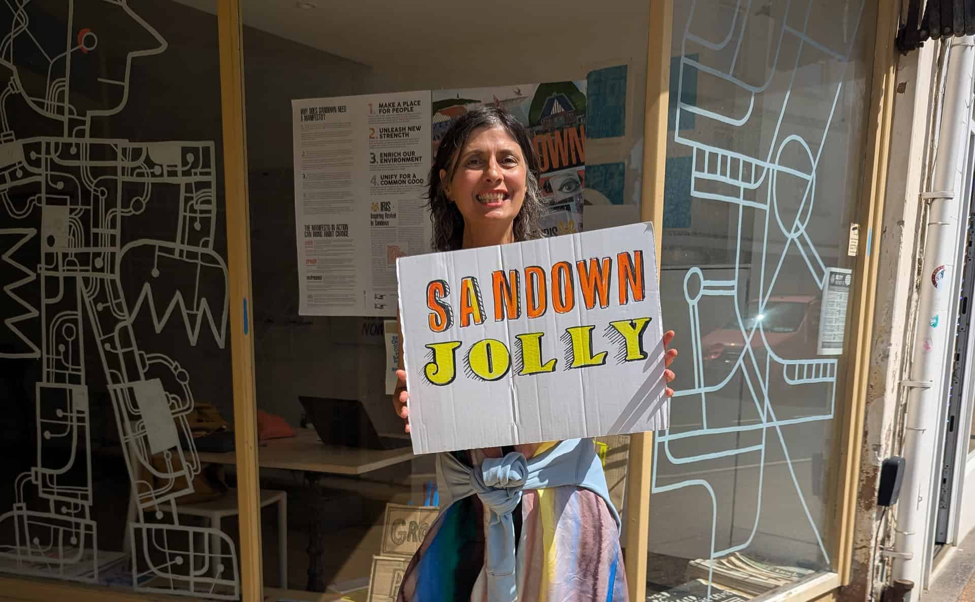 Tracy outside Boojum and Snark with a sign that reads 'sandown jolly'