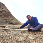 Jack sitting on the beach pointing to some old steel rails