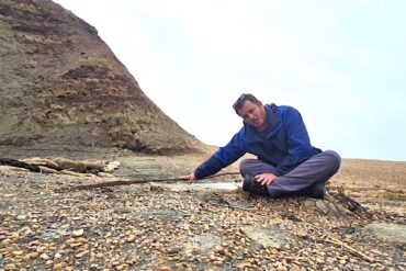 Jack sitting on the beach pointing to some old steel rails