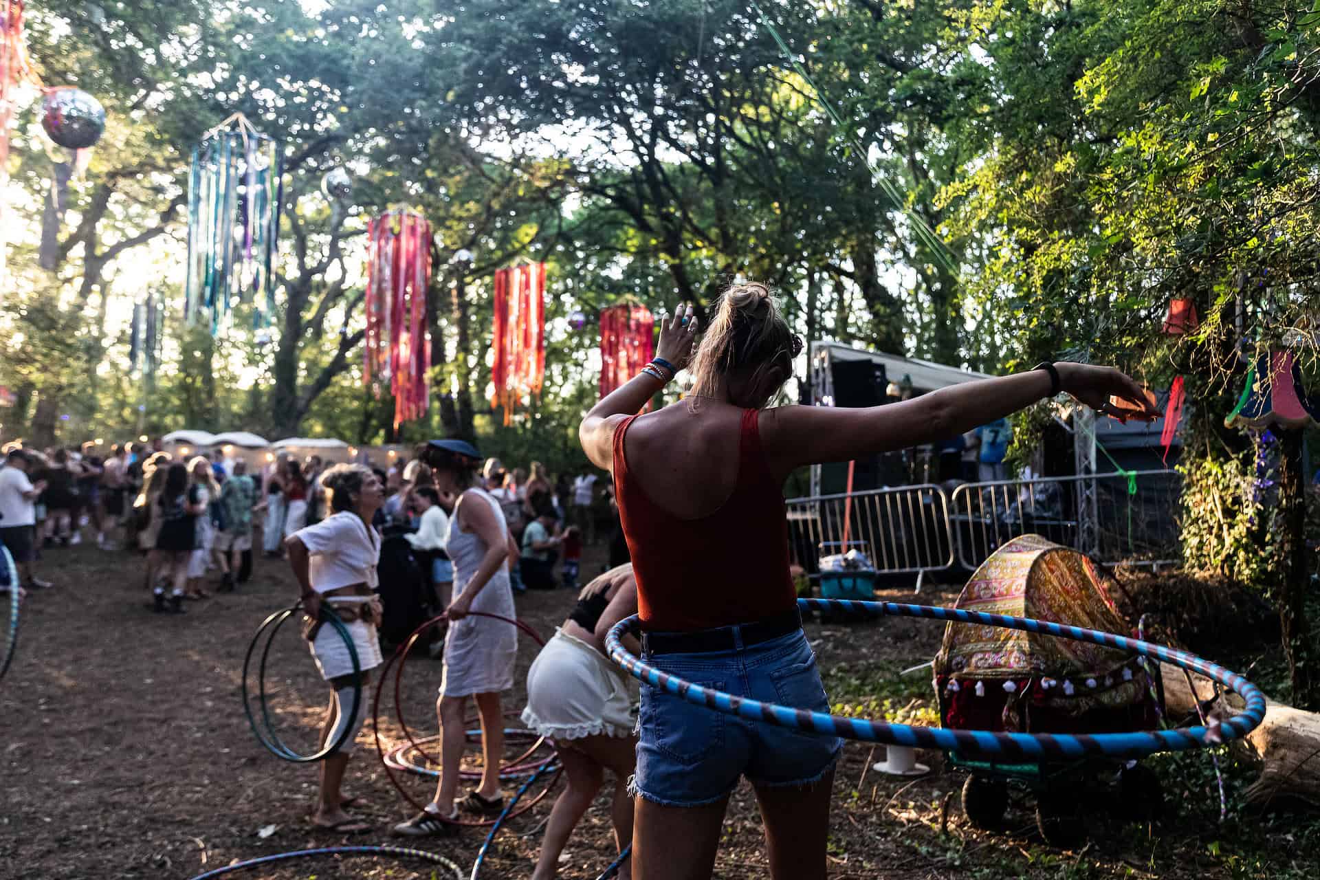People hanging out by the woodland stage during the day, with several people hula hooping