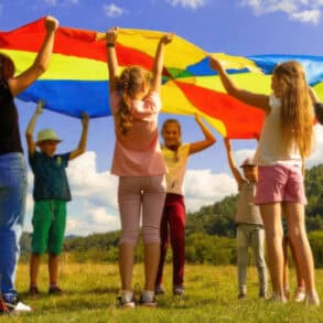 children in a field holding a rainbow blanket in the air