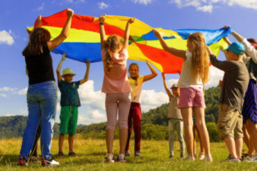 children in a field holding a rainbow blanket in the air