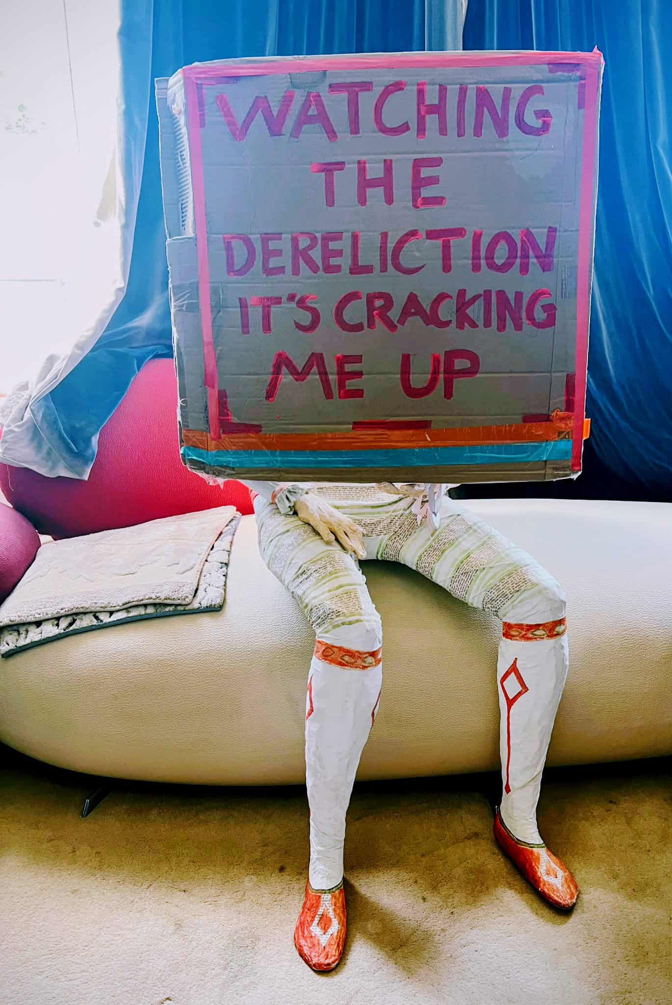 Mannequin hokding a sign that reads "watching the dereliction is cracking me up"