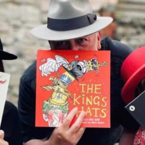 Three people wearing hats and holding hat-related story boks in front of their faces