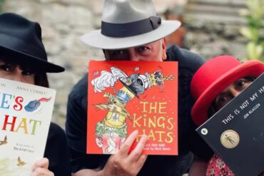 Three people wearing hats and holding hat-related story boks in front of their faces