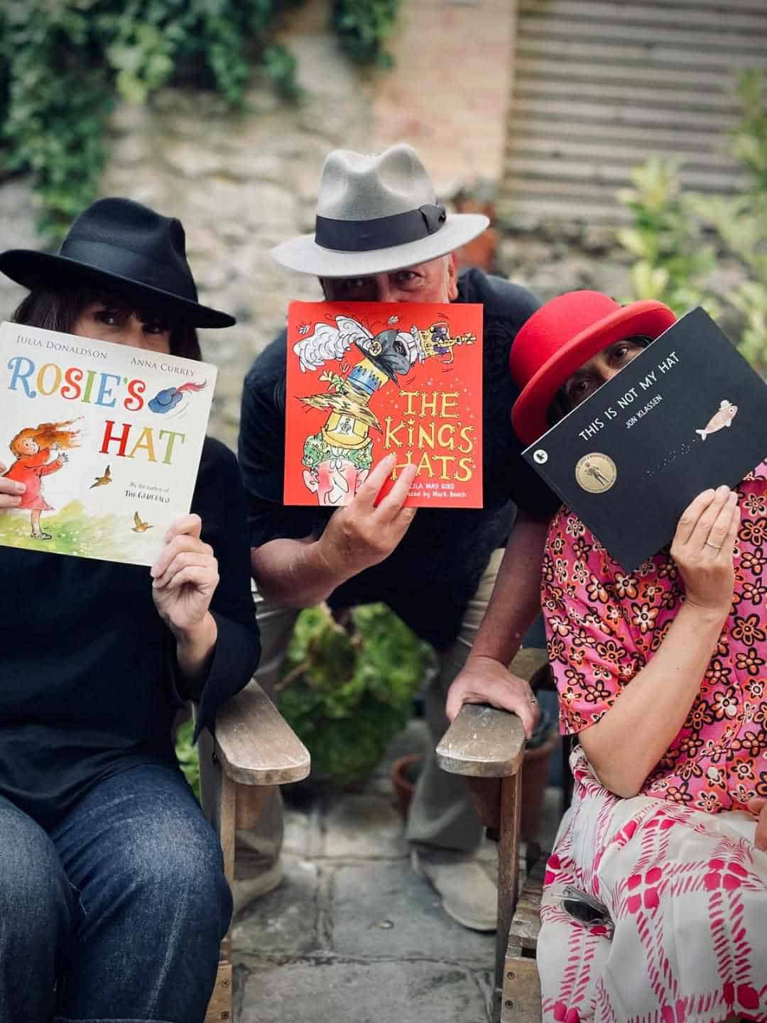 Three people wearing hats and holding hat-related story boks in front of their faces