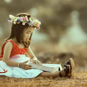 A Child sitting on the grass reading a large book