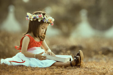 A Child sitting on the grass reading a large book