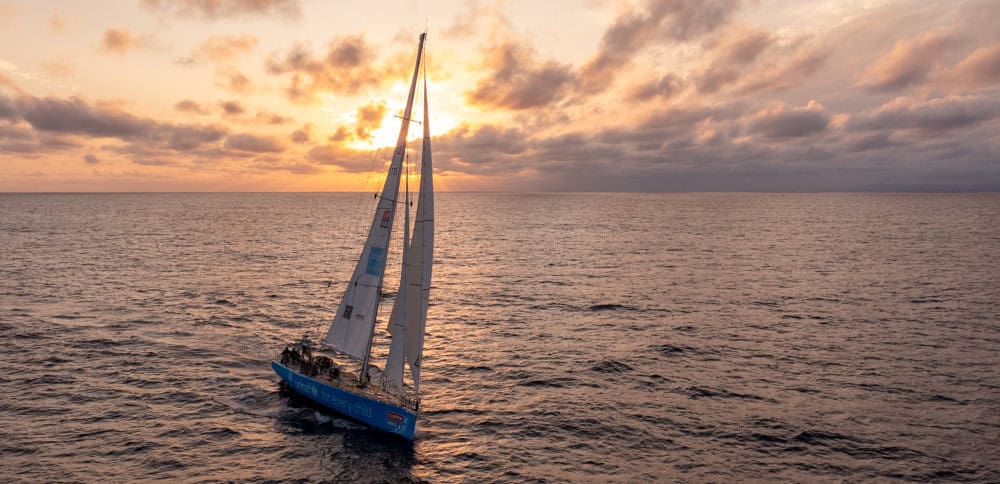 Team UNICEF sailing in the Clipper Race with a peachy coloured sky in the background