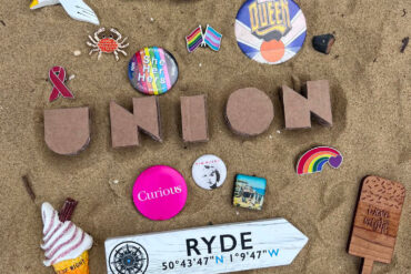 Front cover of Union book, showing sand, ice cream fridge magnet, badge and rainbow pins