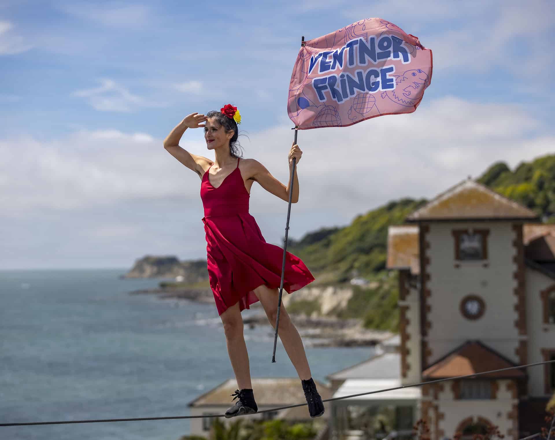 Tightrope walker on a tightrope with Ventnor bay in the background holding a Ventnor fringe festival