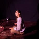 Two dancers sat crossed legged opposite each other on a stage