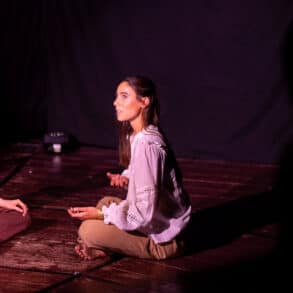 Two dancers sat crossed legged opposite each other on a stage