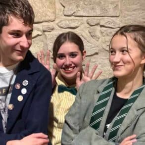 the young Lovestruck Alley performers standing side to side with their arms crossed and one standing behind the other two with waving hands