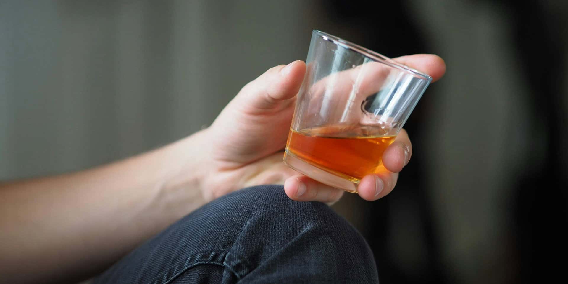 Man in jeans sitting down on the ground with a glass of whisky in his hands