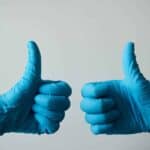 Person wearing surgical gloves holding their thumbs up
