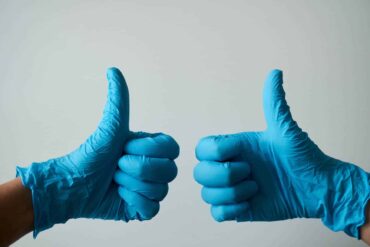 Person wearing surgical gloves holding their thumbs up