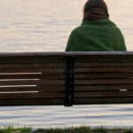 Woman sitting on a park bench looking out onto water