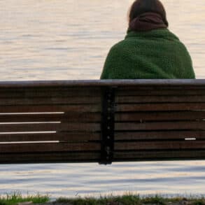 Woman sitting on a park bench looking out onto water