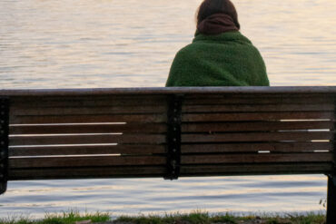 Woman sitting on a park bench looking out onto water