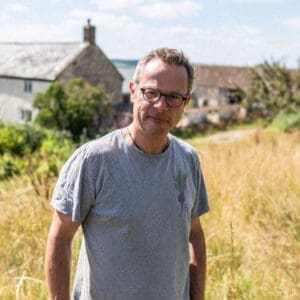 Hugh Fearnley Whittingstall standing in a field with cottages behind him