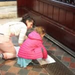 Mother and child doing frottage rubbings of the metal grills on the floor