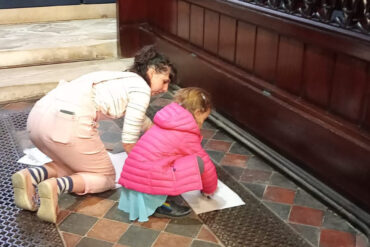 Mother and child doing frottage rubbings of the metal grills on the floor