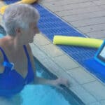 Woman in swimming pool reading instructions from waterproof tablet