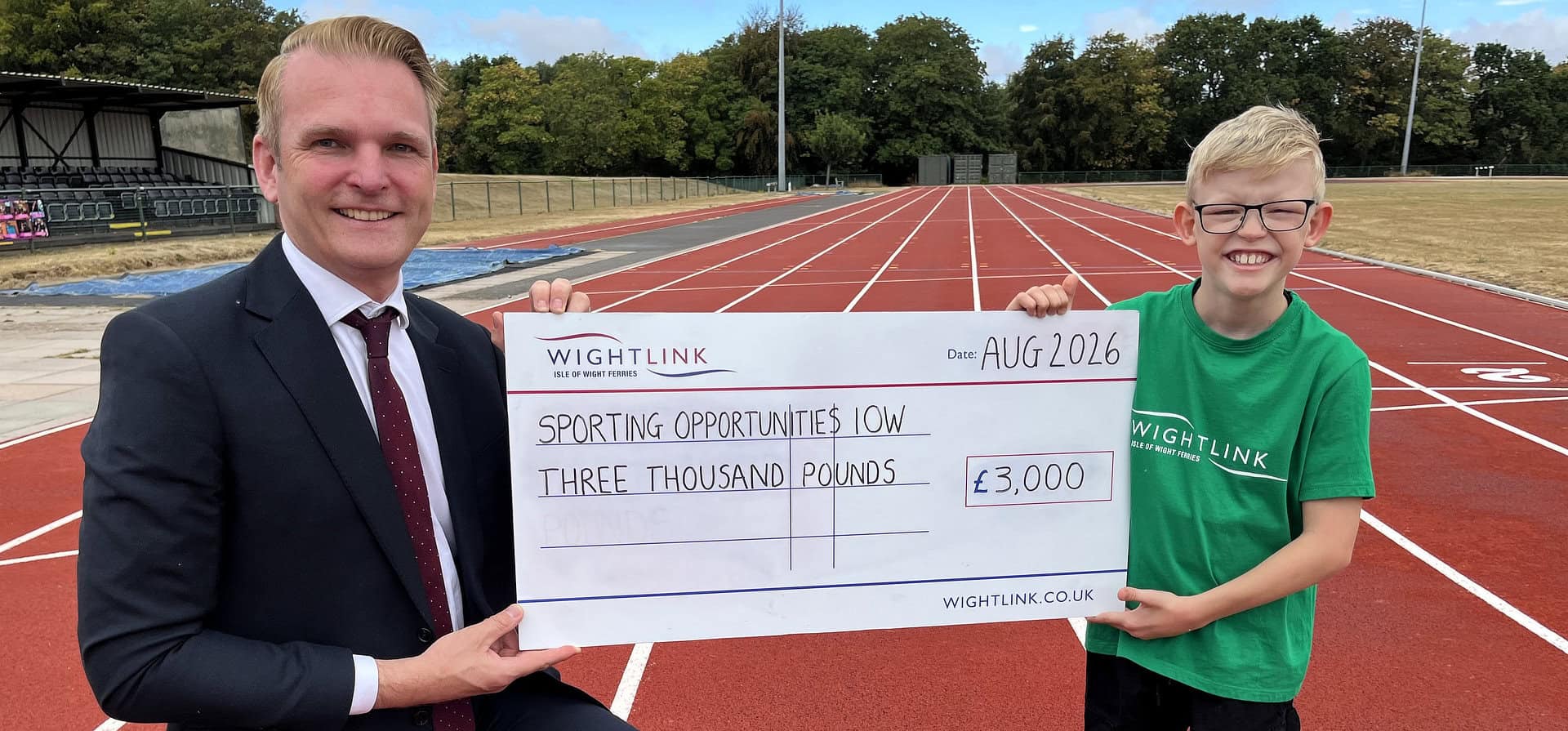 Jake holding a giant cheque with Steve Exley on the running track