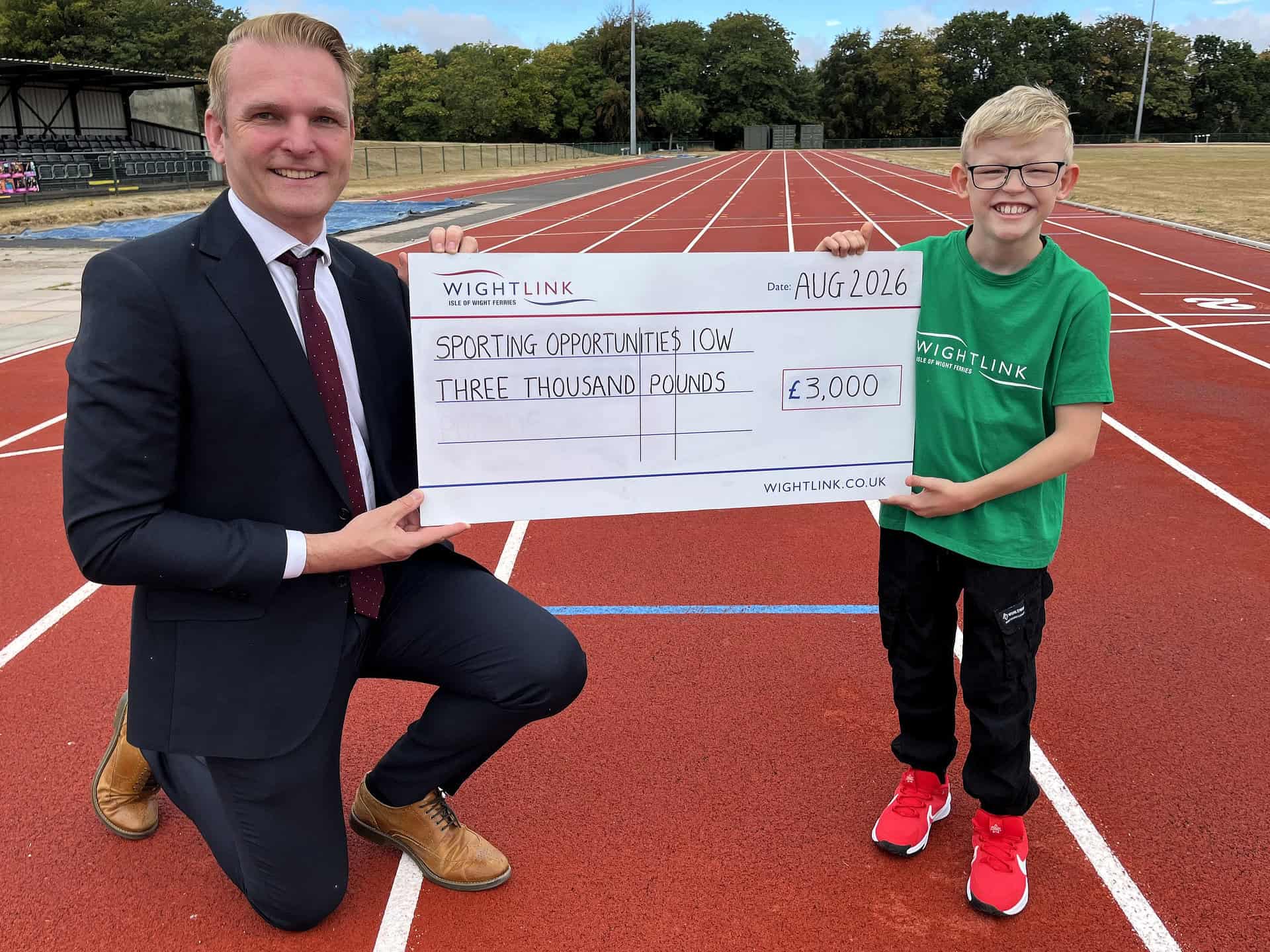 Jake holding a giant cheque with Steve Exley on the running track