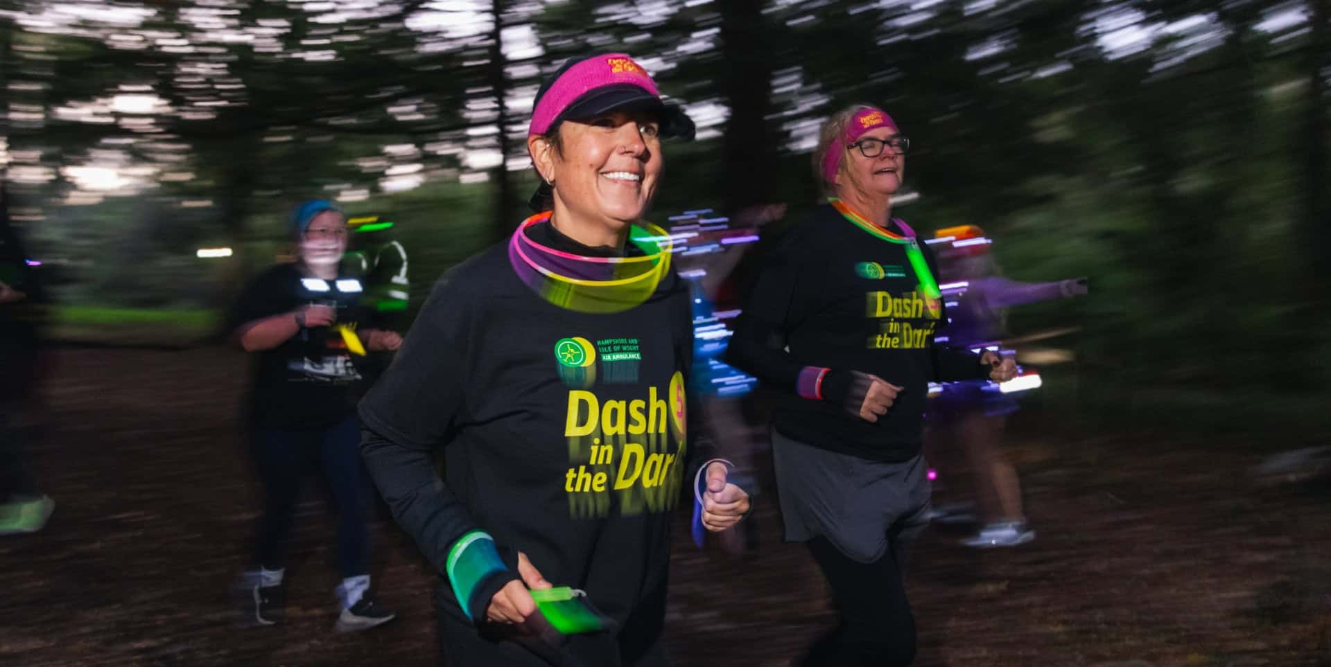 Runners dressed in Dash in the Dark tops running through a park