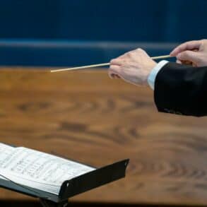conductor holding his baton with sheet music in front of him by winston chen