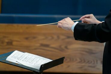 conductor holding his baton with sheet music in front of him by winston chen