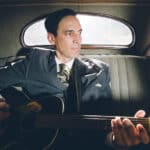 Man in uniform sitting in the backseat of a vintage car with his guitar