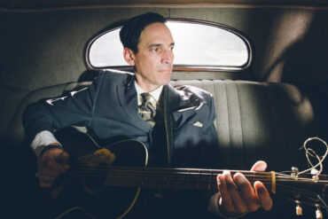 Man in uniform sitting in the backseat of a vintage car with his guitar