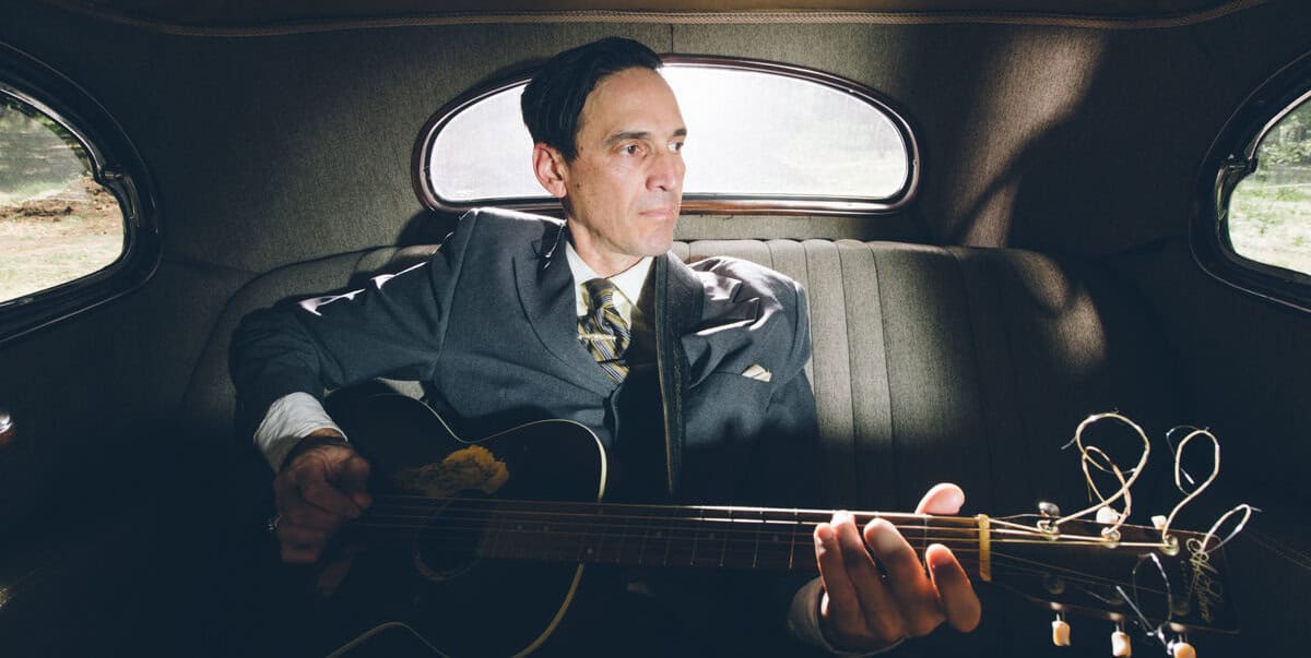 Man in uniform sitting in the backseat of a vintage car with his guitar