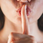 woman with her finger to her mouth in shh-ing motion