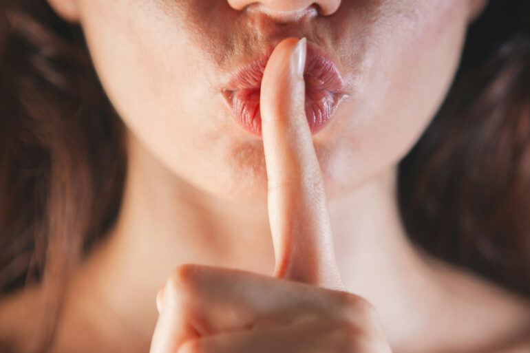 woman with her finger to her mouth in shh-ing motion